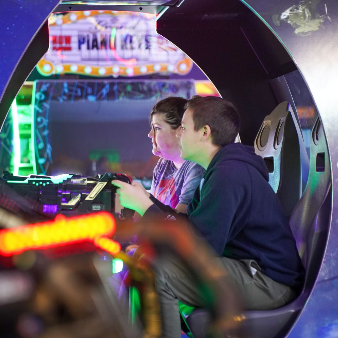Friends playing on a large shooter arcade machine.